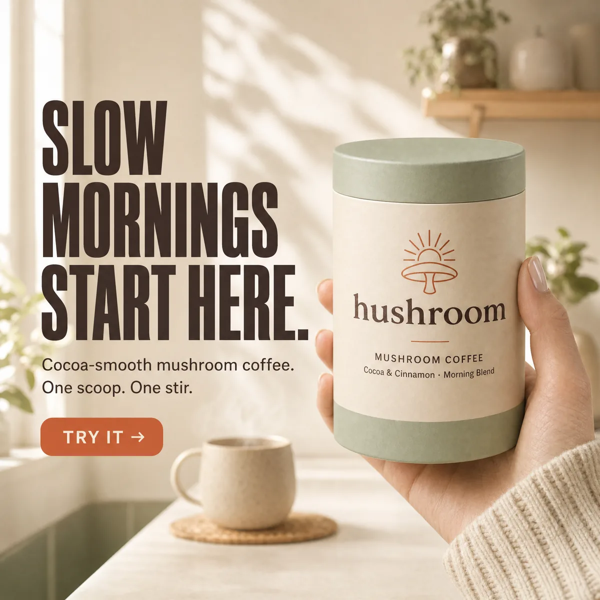 A hand in a cream knit sleeve holds a sage-and-oat Hushroom mushroom coffee canister up to the camera in a sunlit kitchen.